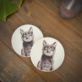 Two round coasters featuring a printed illustration of a black cat with green eyes, displayed on a rustic wooden tabletop.