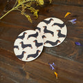 Two round coasters with a Black and Tan dachshund pattern, displayed on a rustic dark wood surface with dried flowers.