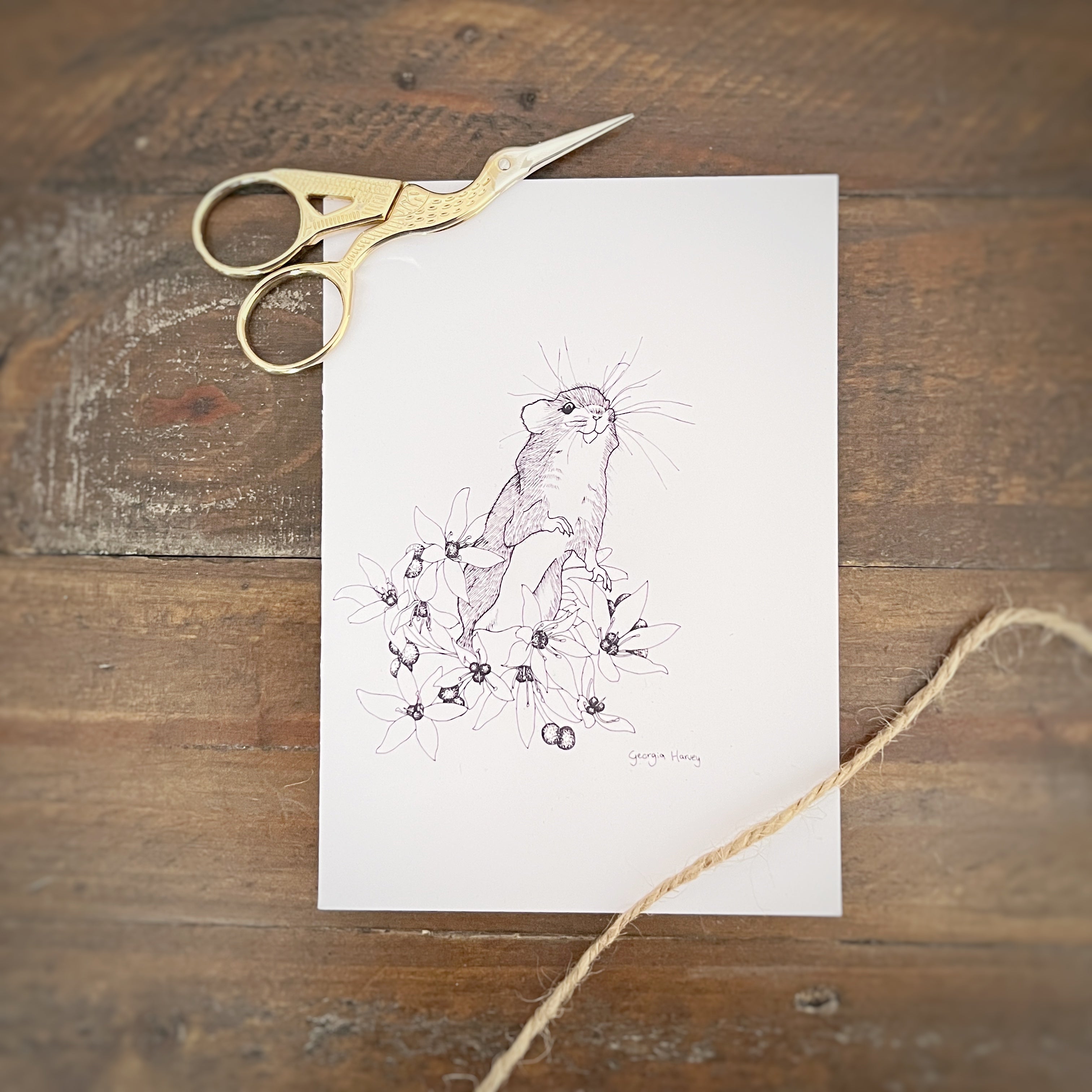 Whimsy handmade postcard with a black and white field mouse on flowers with scissors and string around it with a wooden background